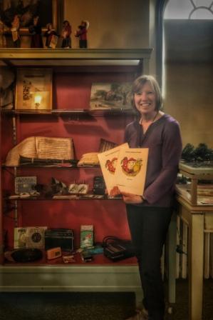 Sheila Cooke-Kayser, retired National Park Service ranger next to museum exhibit holding history activity book “Our Town”